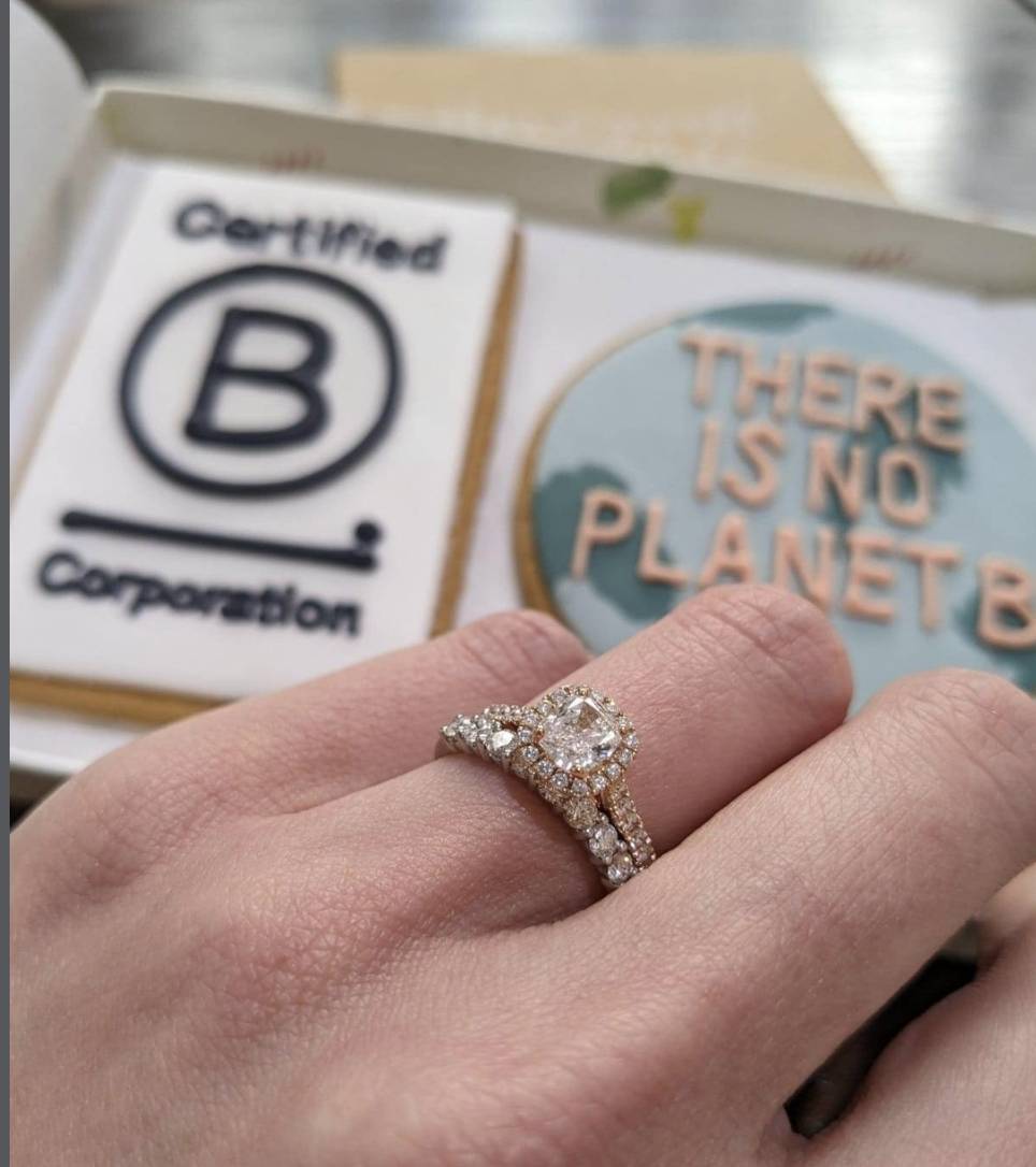 An ethical engagement ring on a hand with Certified B Corporation and 'There is no planet B' cookies