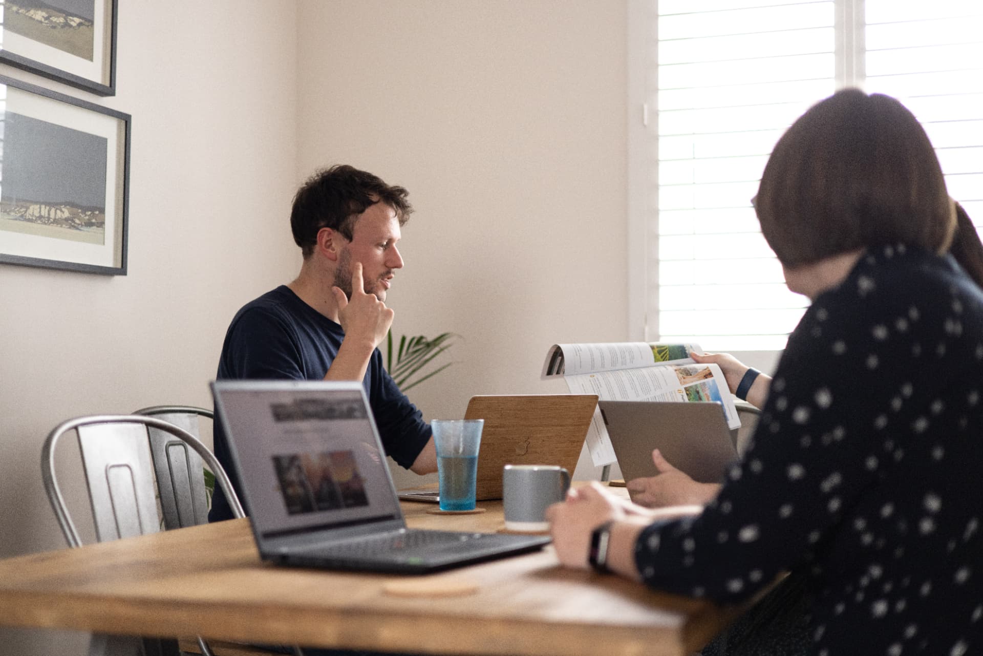 Two Madhatter team members reviewing a printed magazine spread at a sunlit table