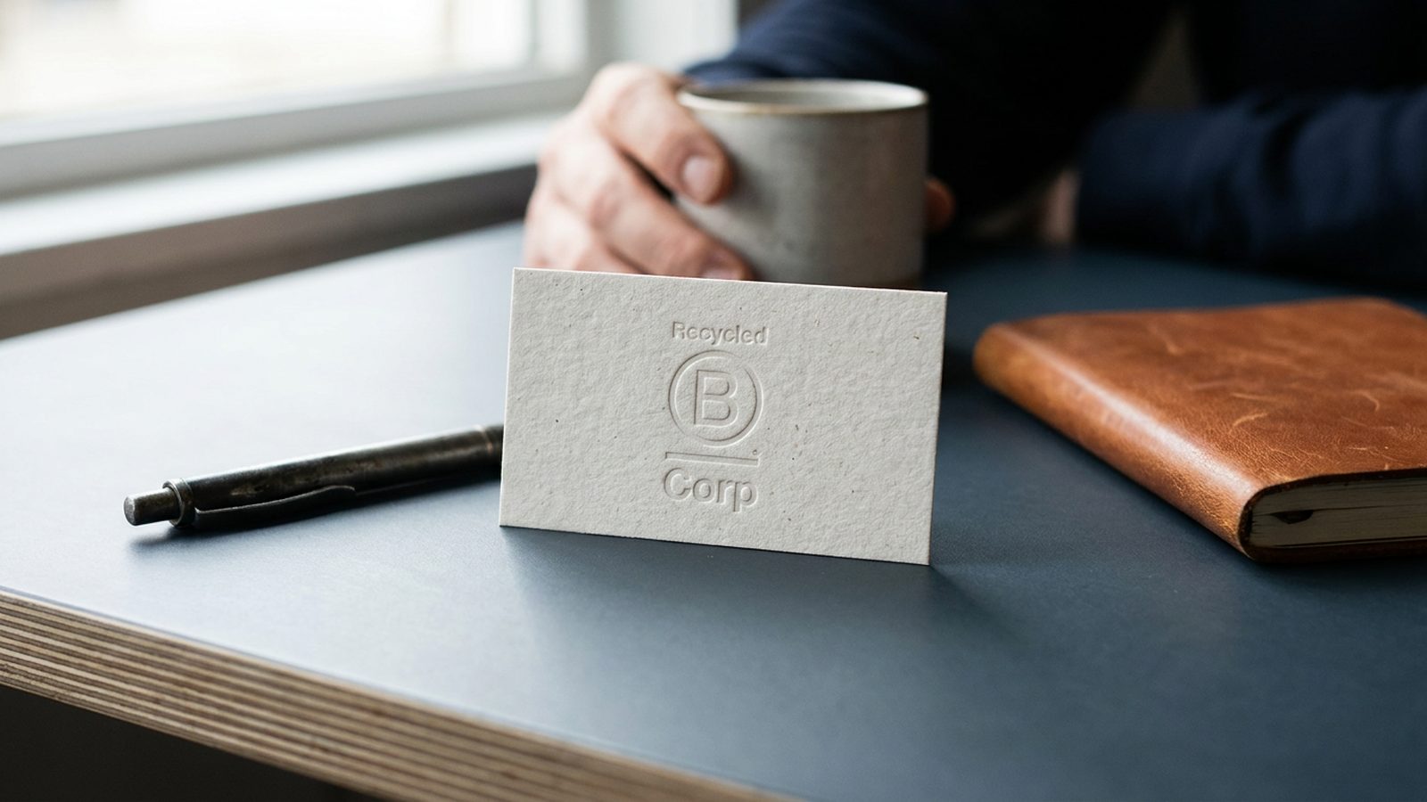 A B Corp certification logo is subtly embossed onto a business card on a minimalist desk.