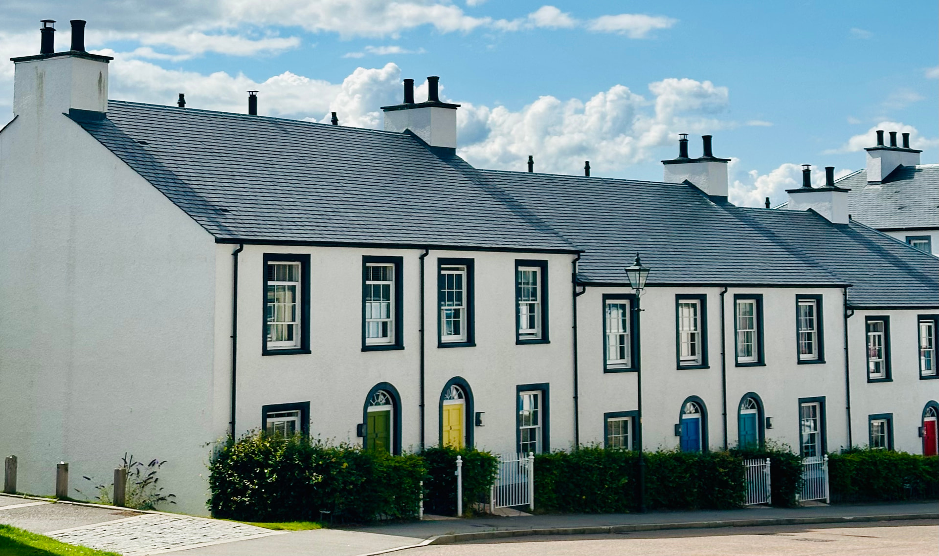 A terrace of white Tornagrain houses with green, yellow, blue and red front doors